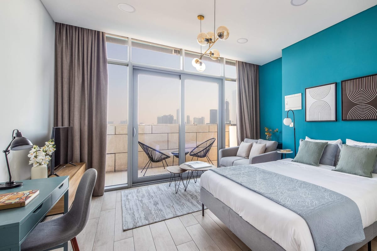 A modern hotel room with a large bed, a desk, and a balcony with a city view.