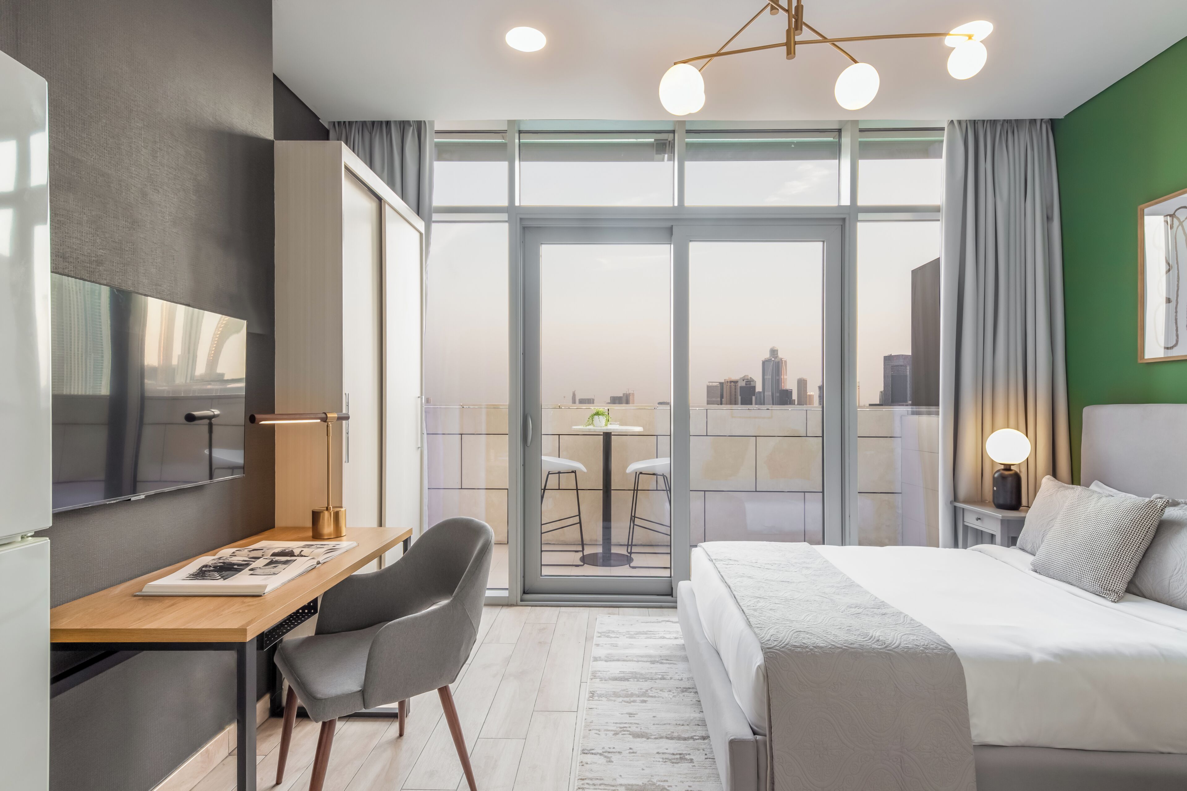 Ein modernes Hotelzimmer mit einem großen Bett, einem Schreibtisch mit Stuhl, einem Fernseher und einem Balkon mit Blick auf die Stadt.