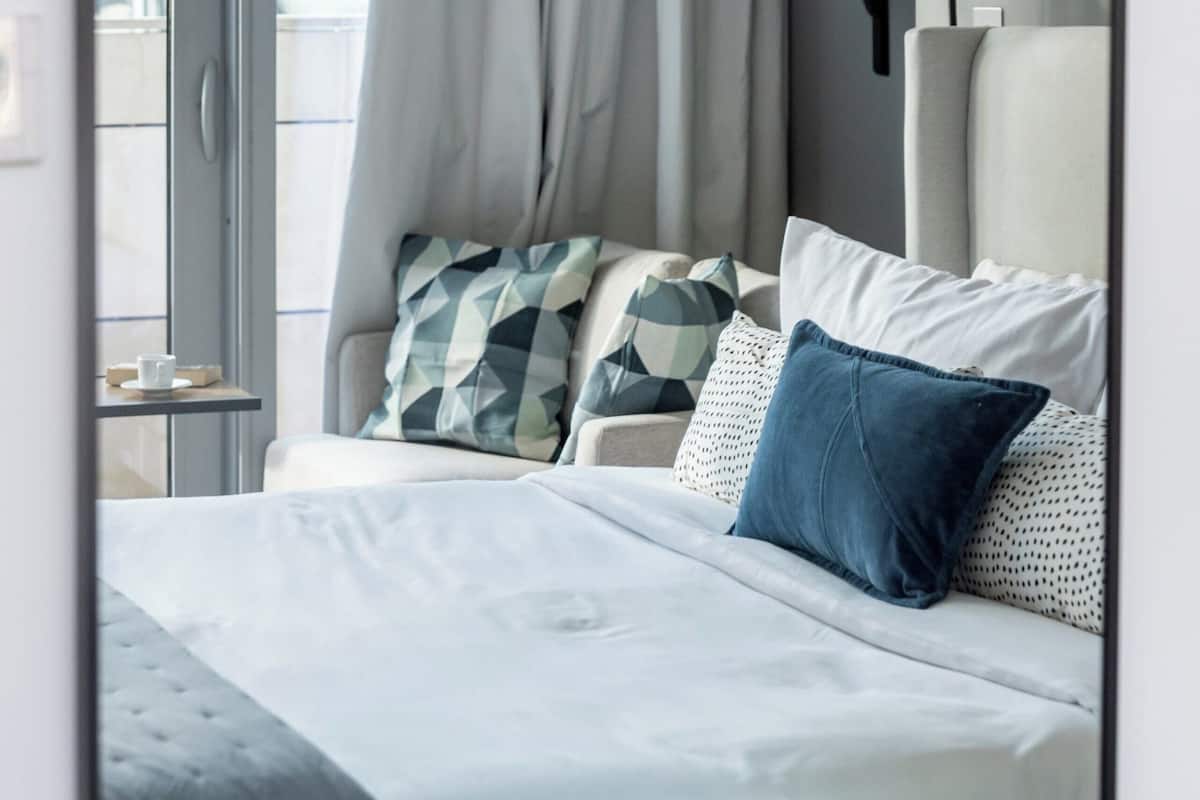 A neatly arranged bedroom with a bed, pillows, a bedside table, and a lamp.