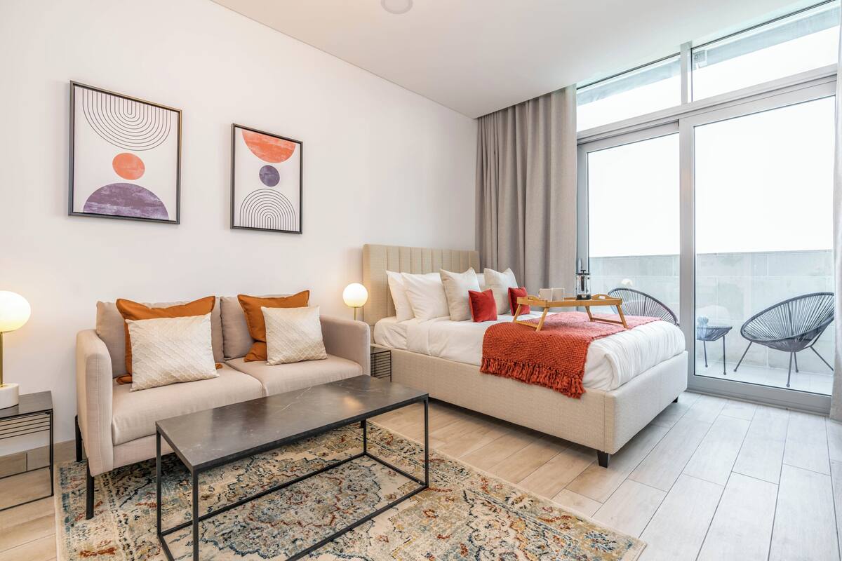A modern hotel room with a sofa, a bed, a coffee table, and a large window with a view.