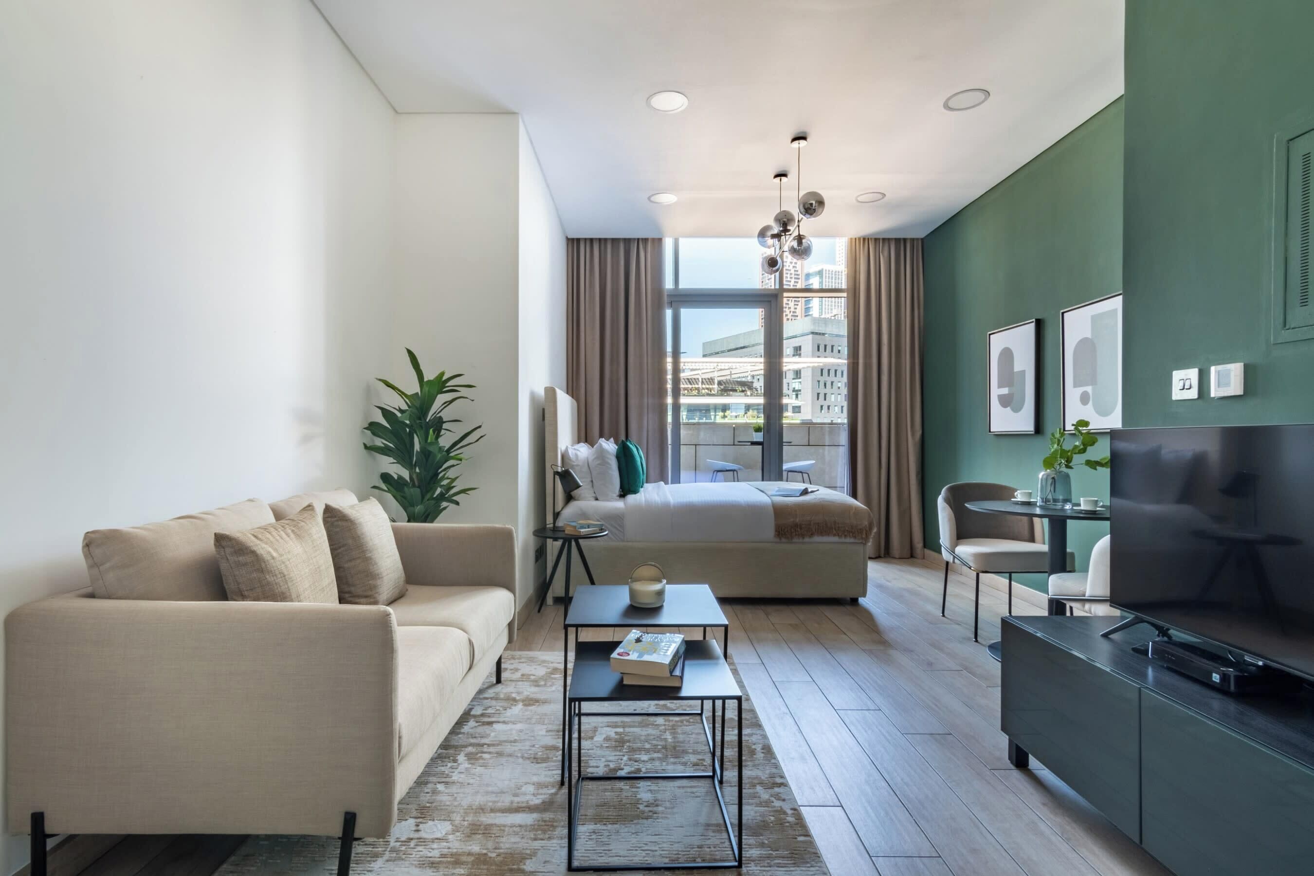 Ein modernes Wohnzimmer mit einer Couch, einem Couchtisch und einer TV-Konsole. Im Hintergrund ist ein Bett mit Blick auf die Stadt zu sehen.