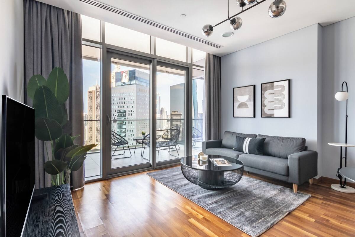 A modern living room with a grey sofa, a coffee table, and a large window with a city view.