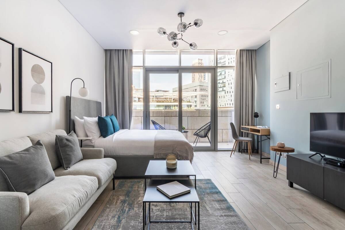 A modern hotel room with a large bed, a sofa, a desk, and a TV.