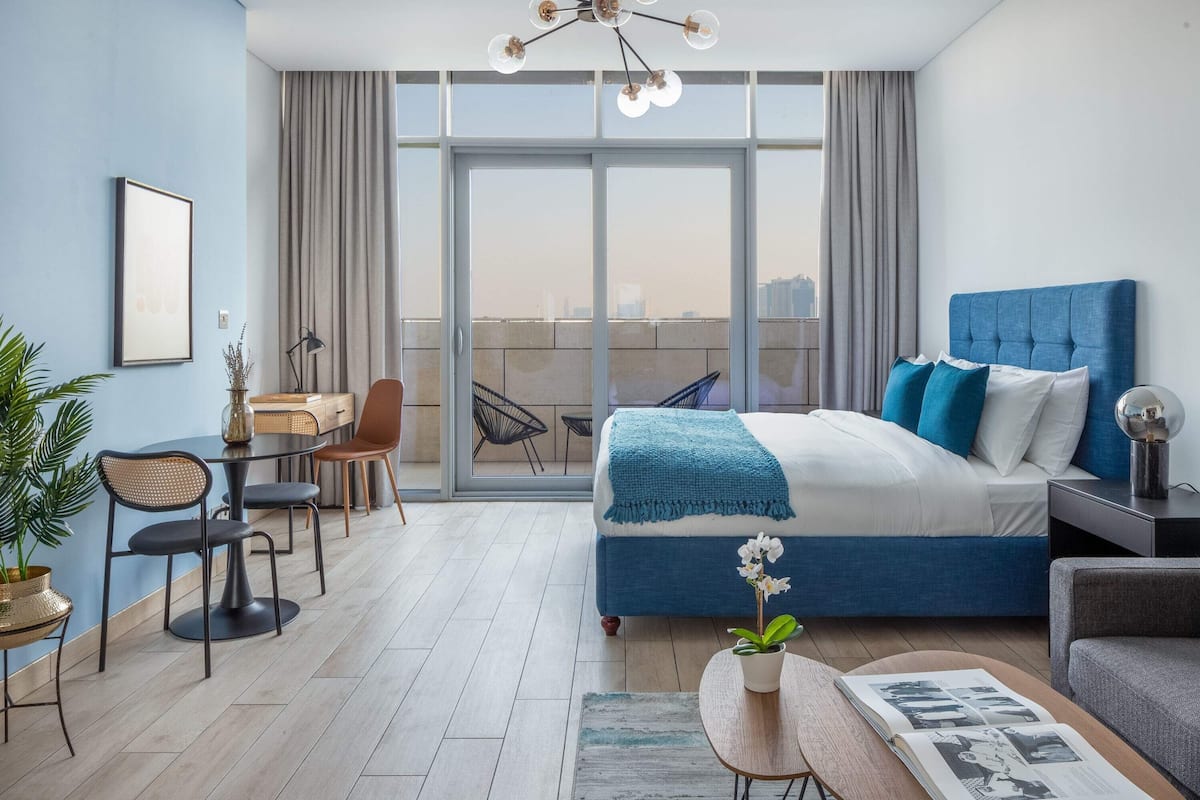 A modern bedroom with a large bed, a dining area, and a balcony with a city view.