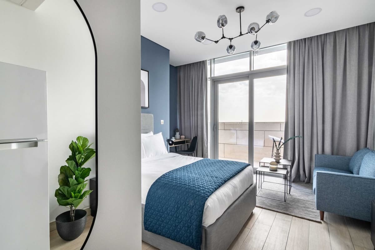 A modern hotel room with a bed, a desk, a chair, a balcony, and a potted plant.