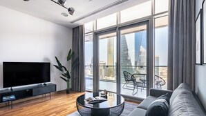 A modern living room with a large flat-screen TV, a round coffee table, a sofa, and a balcony with a view of the city skyline. - Burj Daman (Dubai)