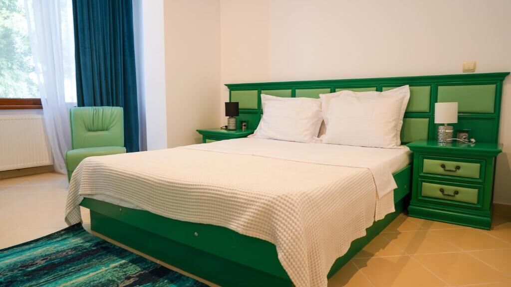 A bed with a green headboard, white bedding, and two bedside tables with lamps.