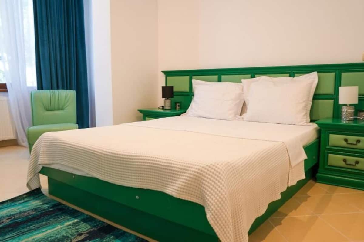 A bed with a green headboard, white bedding, and two bedside tables with lamps.
