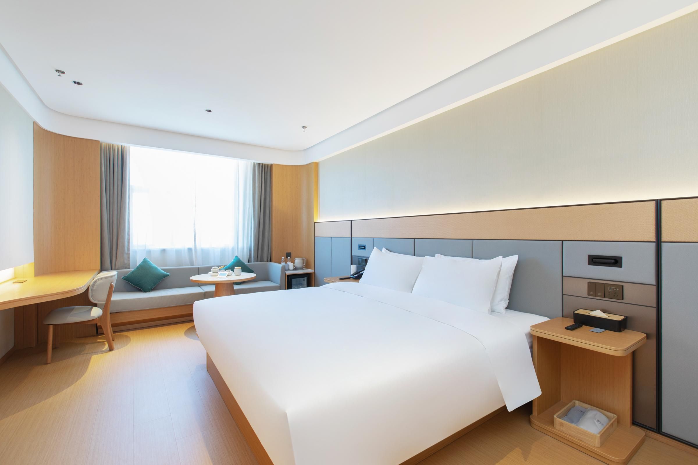 Una habitación de hotel con una cama grande, un escritorio, una silla, una mesita pequeña y una mesita de noche.