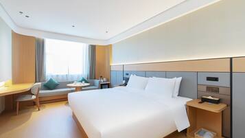 Una habitación de hotel con una cama grande, un escritorio, una silla, una mesita pequeña y una mesita de noche.