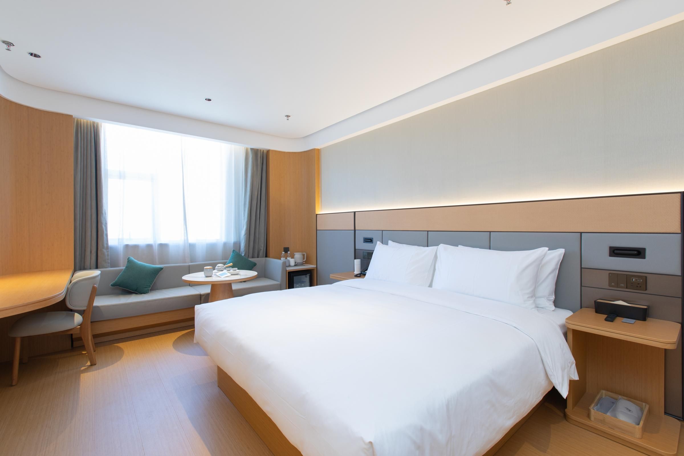 Una habitación de hotel moderna con una cama grande, un sofá, una mesita y una mesita de noche.
