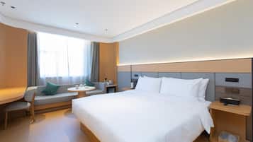 A modern hotel room with a large bed, a sofa, a small table, and a nightstand.