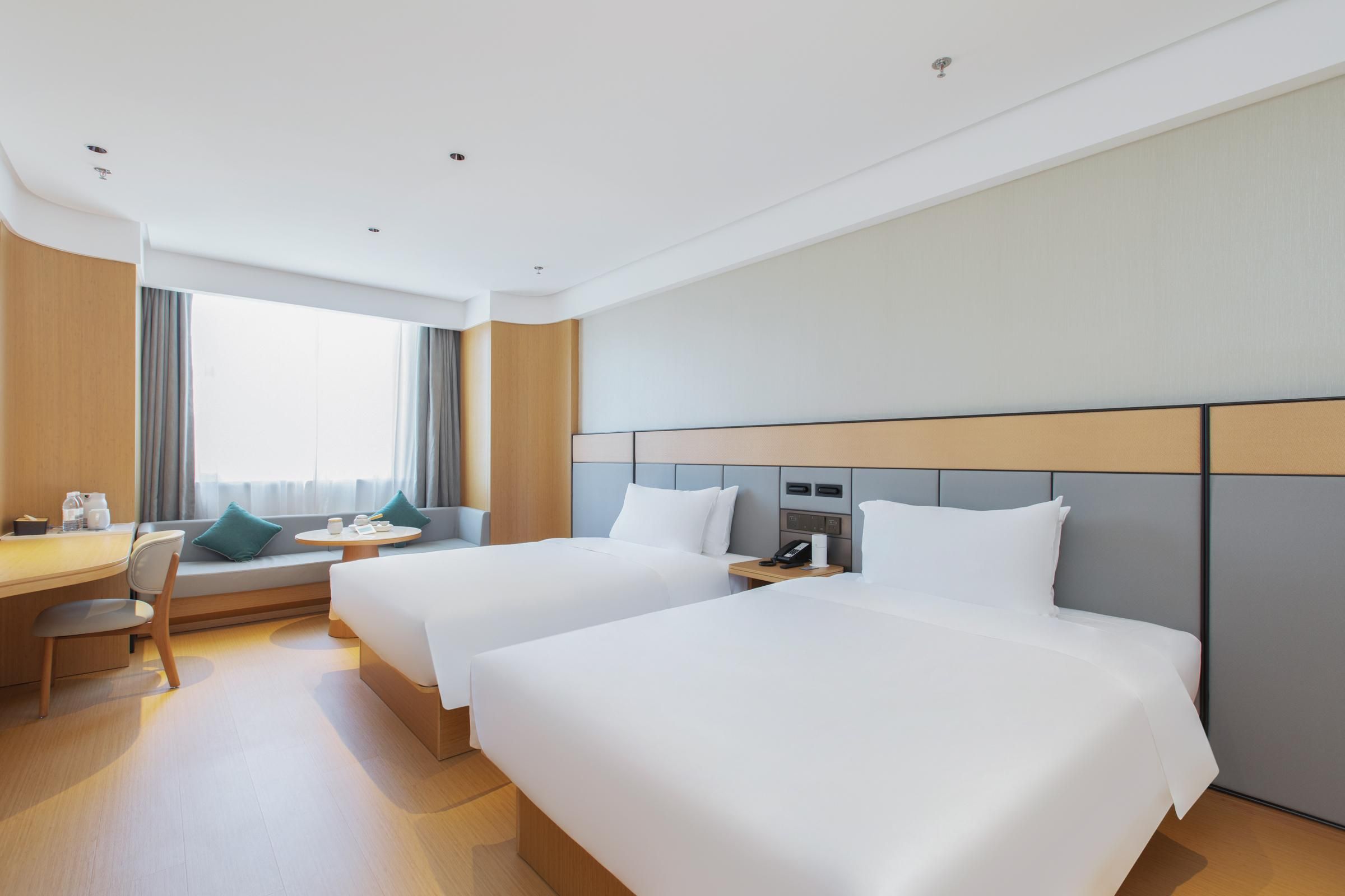 Una habitación de hotel con dos camas, un escritorio, una silla, una mesita y una ventana con cortinas.