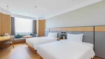 Una habitación de hotel con dos camas, un escritorio, una silla, una mesita y una ventana con cortinas.