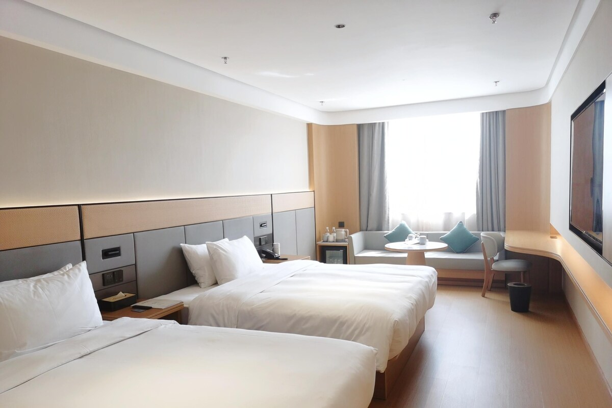 A hotel room with two beds, a sofa, a small table, and a TV.