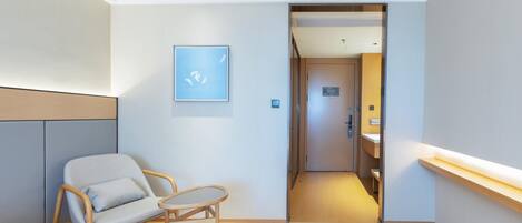 A hotel room with a wooden chair, a small table, a framed picture on the wall, and a door leading to a bathroom.