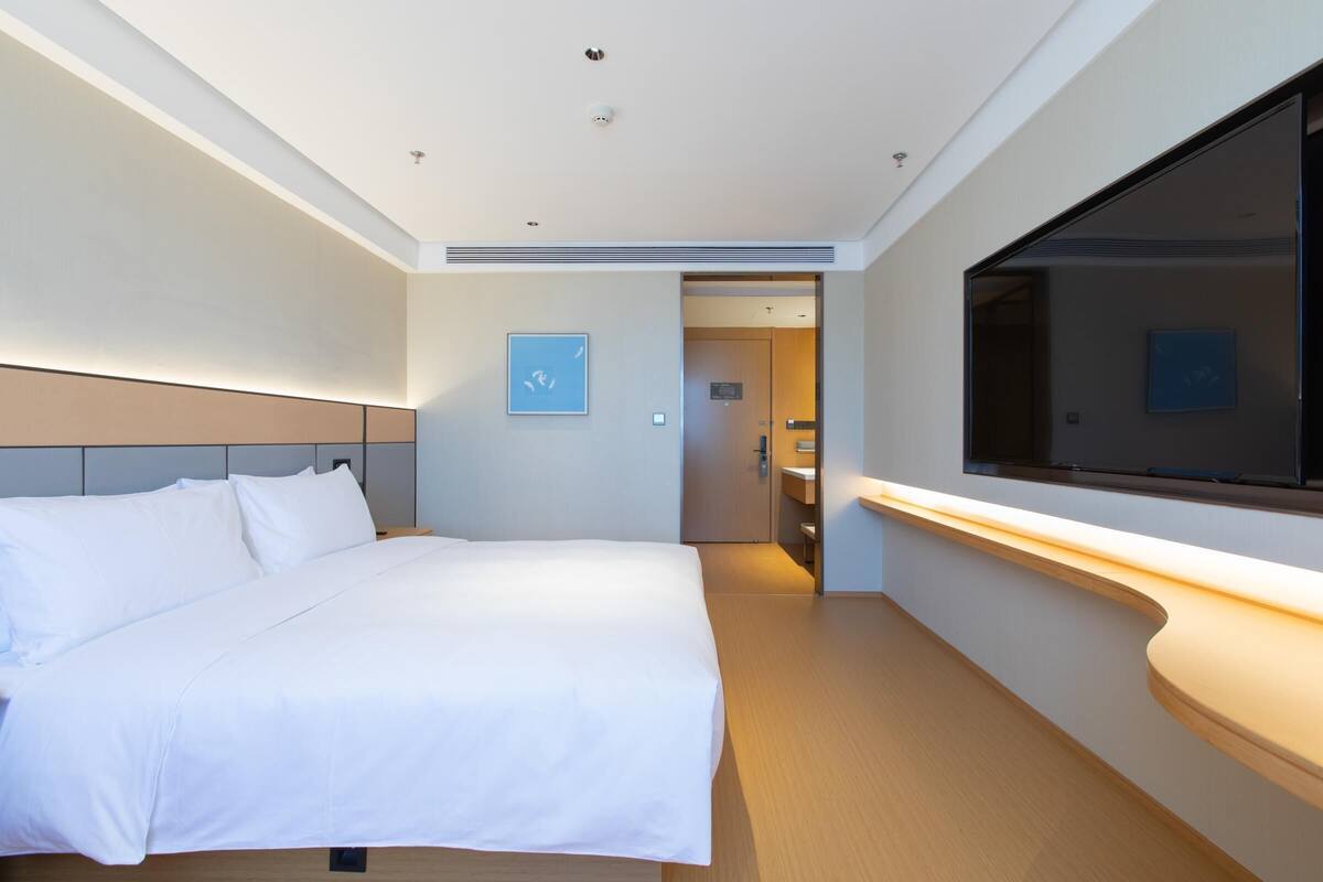 Una habitación de hotel moderna con una cama grande, un televisor de pantalla plana, una mesita de noche y una puerta que da a un baño.