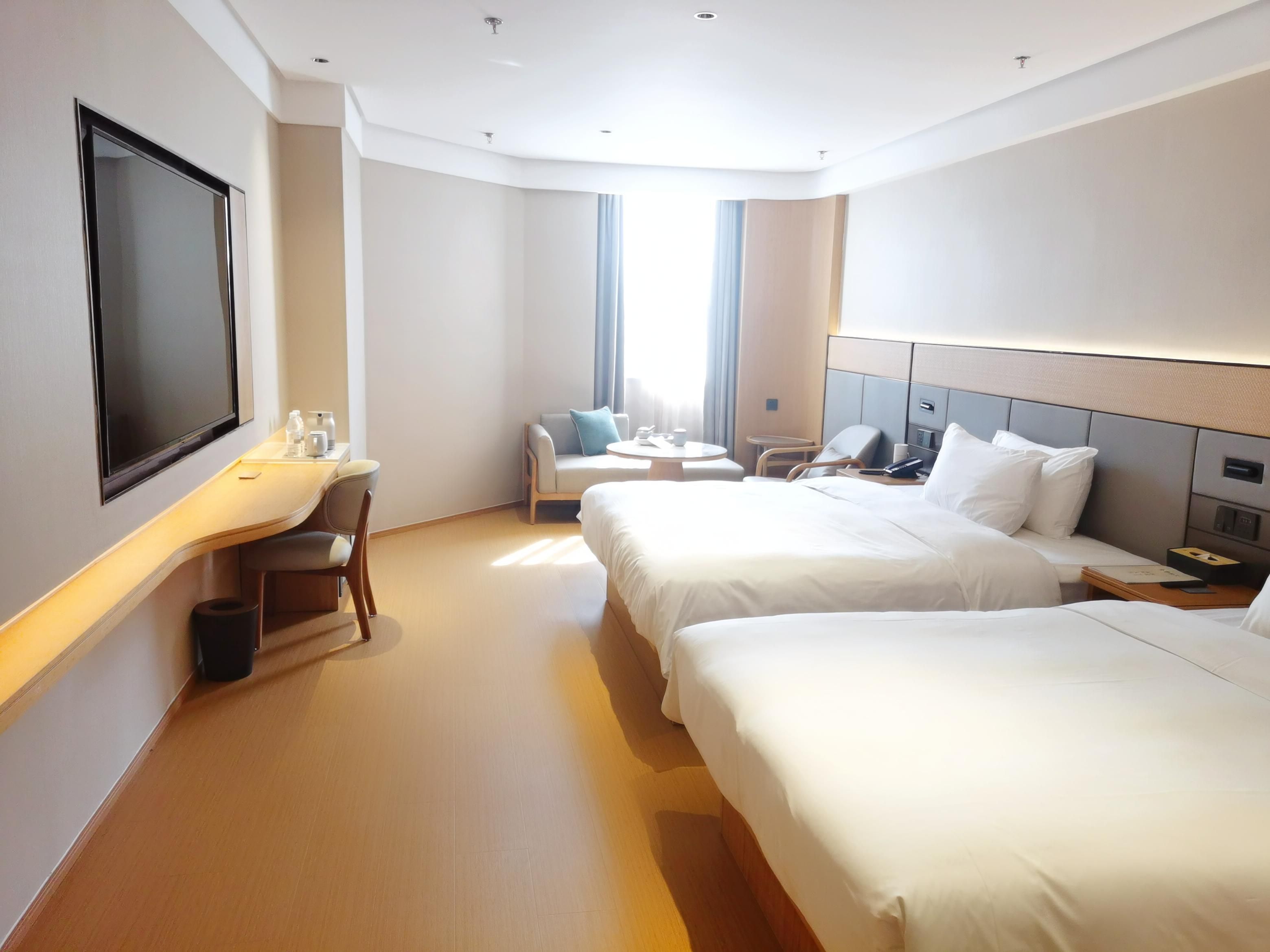 Habitación de hotel con dos camas, un escritorio con silla, televisión y ventana con cortinas.