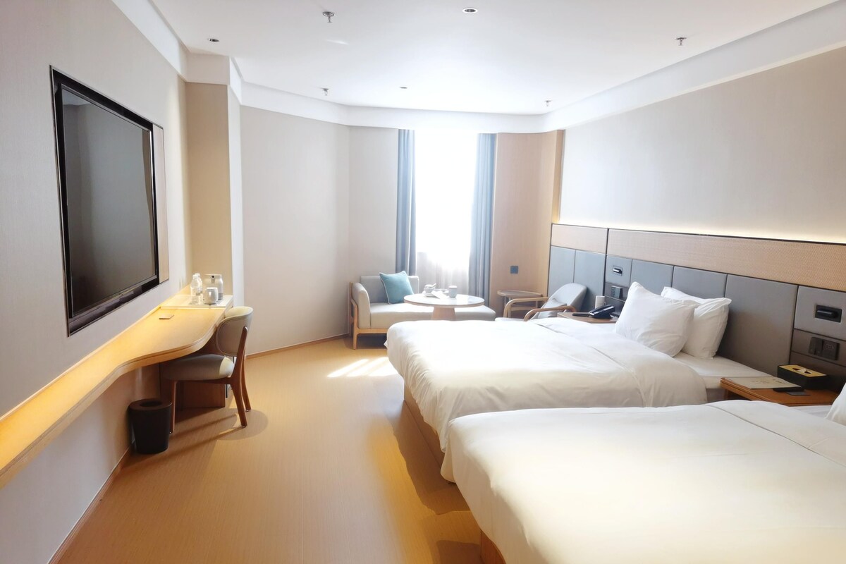 Ett hotellrum med två sängar, ett skrivbord med en stol, en TV och ett fönster med gardiner.