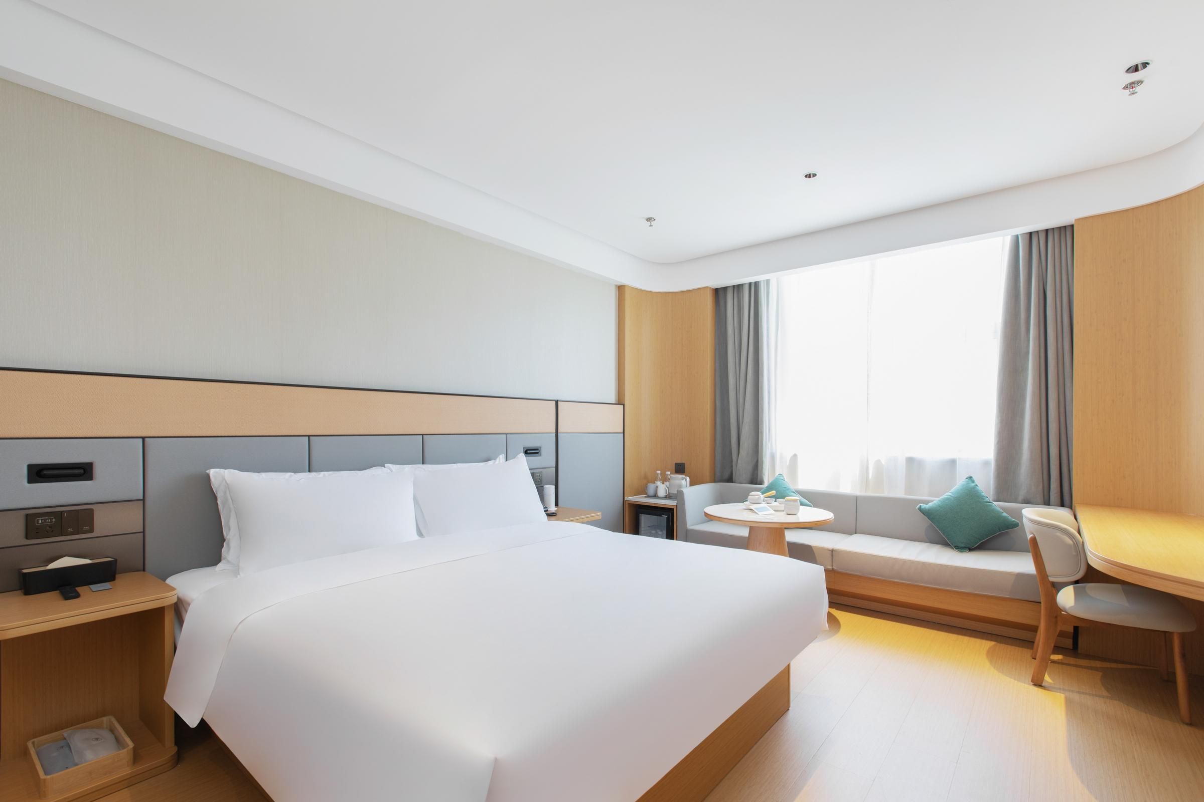A hotel room with a large bed, a small table, a sofa, and a window with curtains.