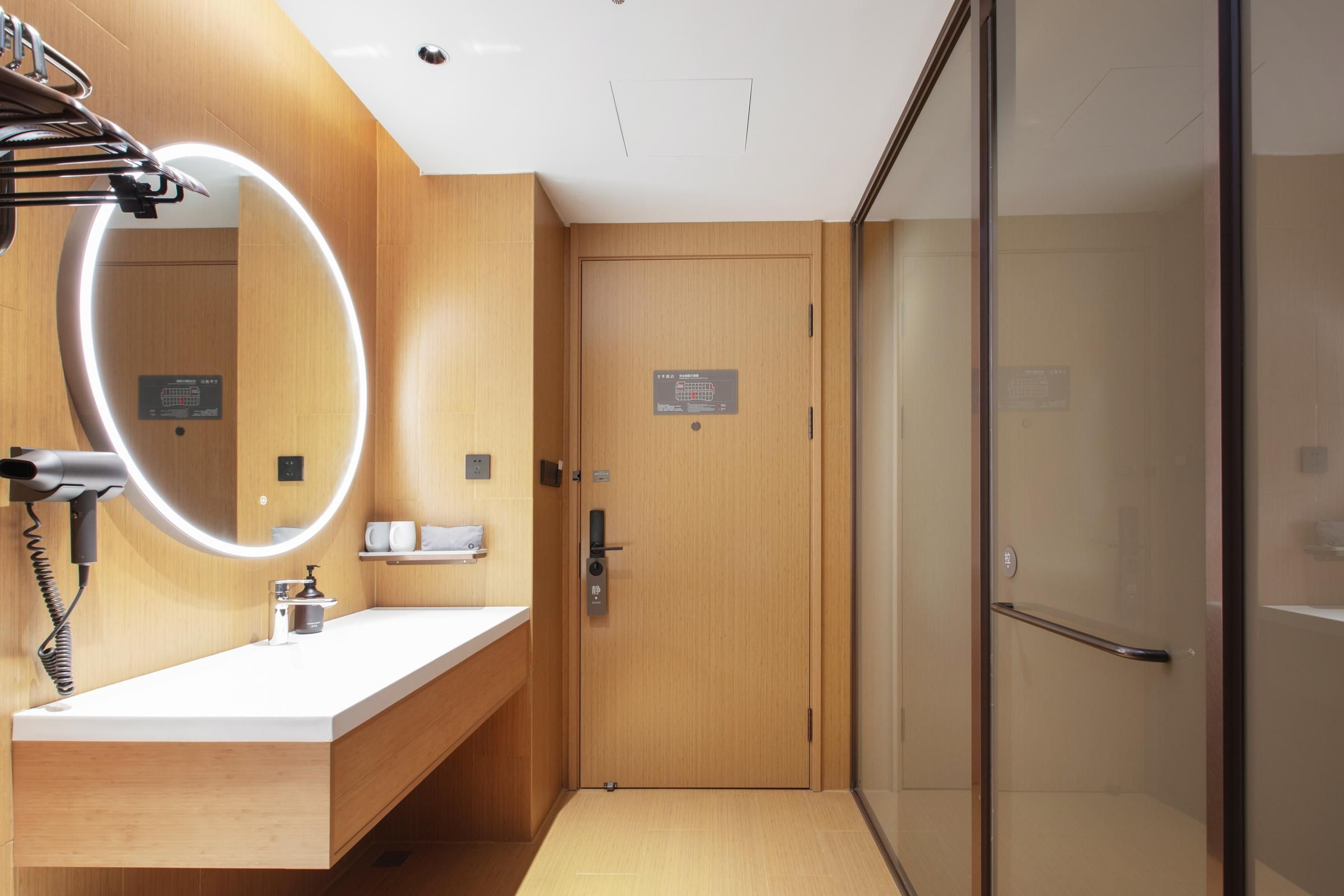 A modern bathroom with a wooden vanity, a mirror with lights, a shower, and a glass door.