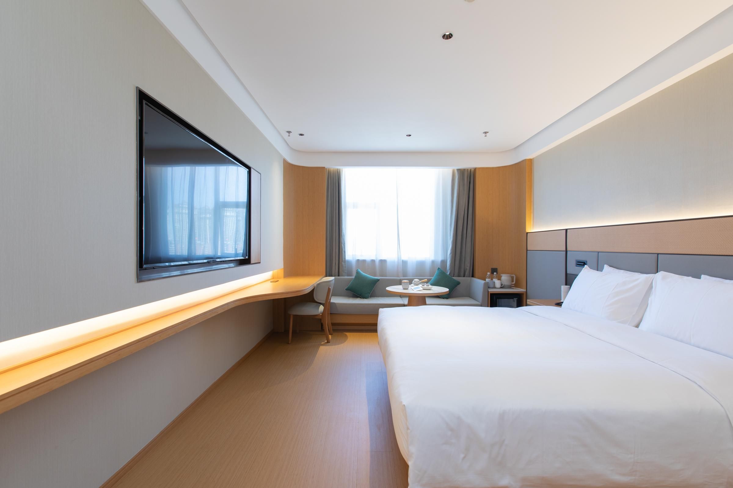 A hotel room with a bed, a desk, a chair, a small table, and a window.