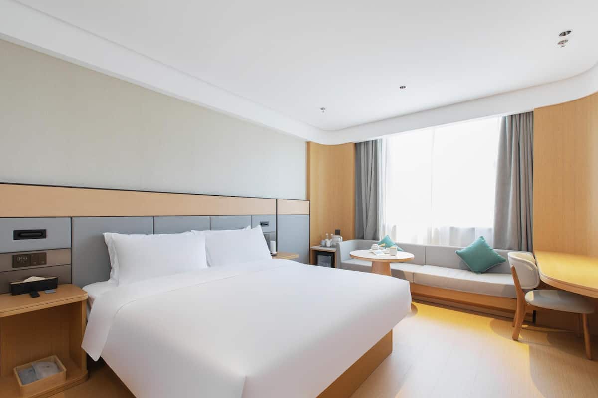 Una habitación de hotel con una cama grande, una mesita, un sofá y una ventana con cortinas.