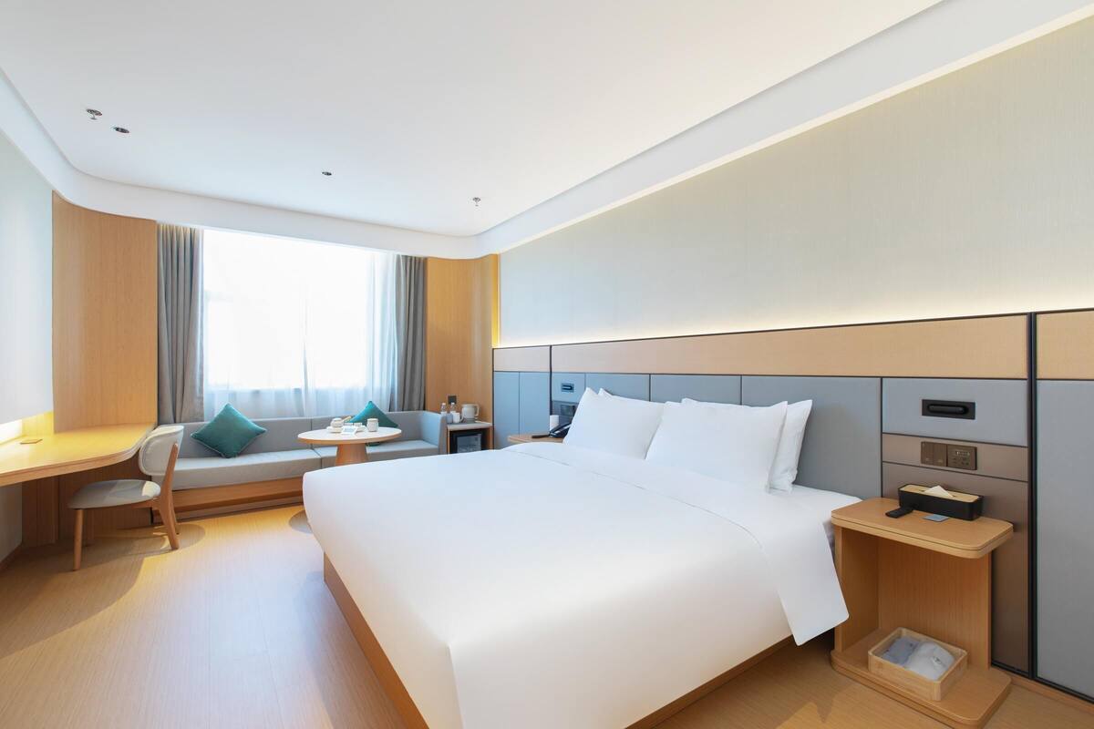Una habitación de hotel con una cama grande, un escritorio, una silla, una mesita pequeña y una mesita de noche.