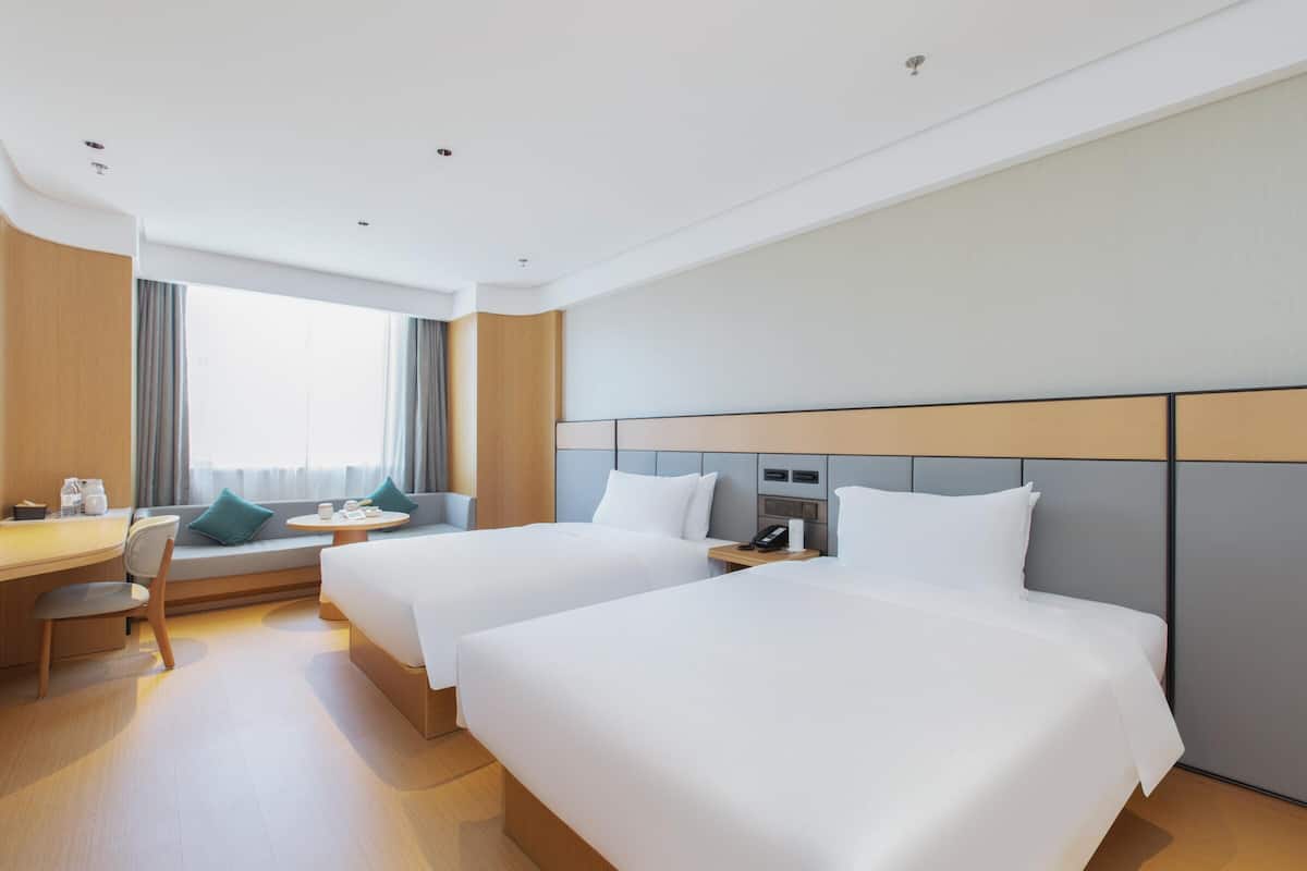 Una habitación de hotel con dos camas, un escritorio, una silla, una mesita y una ventana con cortinas.