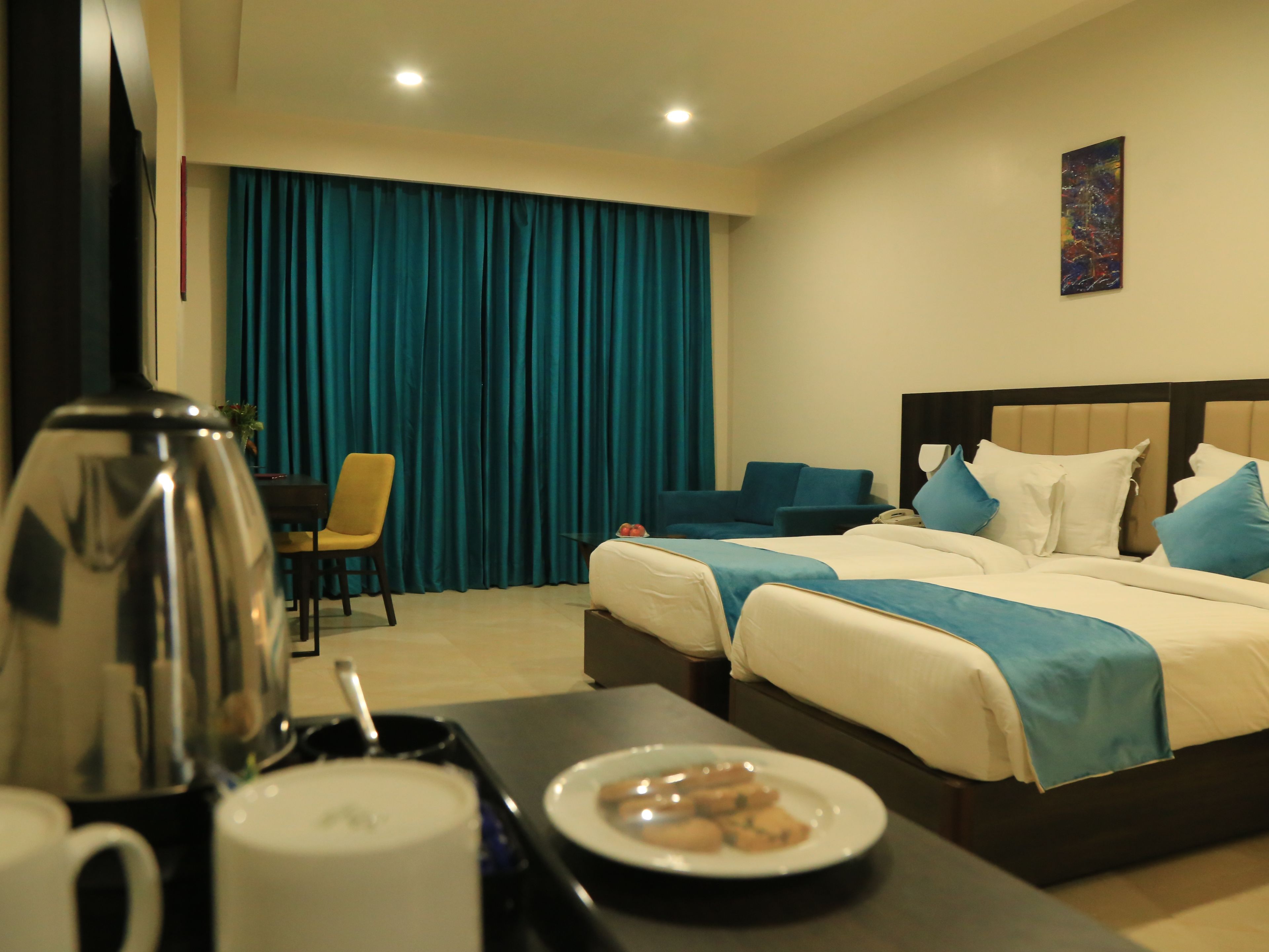 Habitación de hotel con una cama, una mesita de centro con un plato de galletas, una cafetera y una silla.