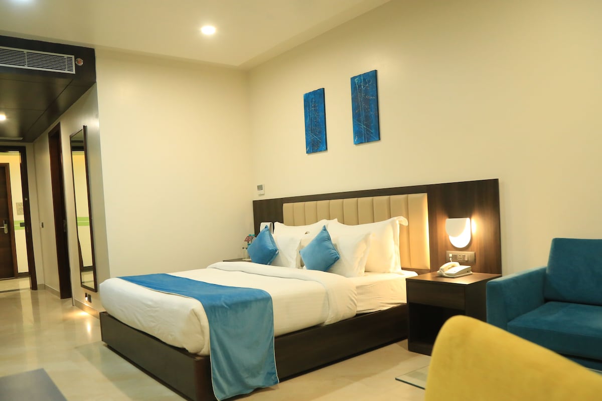 A modern hotel room with a large bed, bedside tables, a chair, and artwork on the wall.