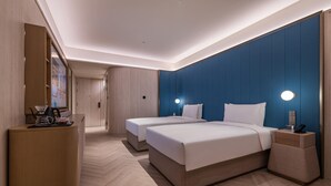 Hotellihuone, jossa on kaksi sänkyä, työpöytä, peili ja seinään kiinnitetty valaisin.