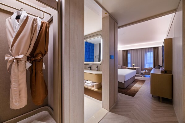 A hotel room with a bed, a desk, a chair, a bathroom with a mirror, and a robe rack.