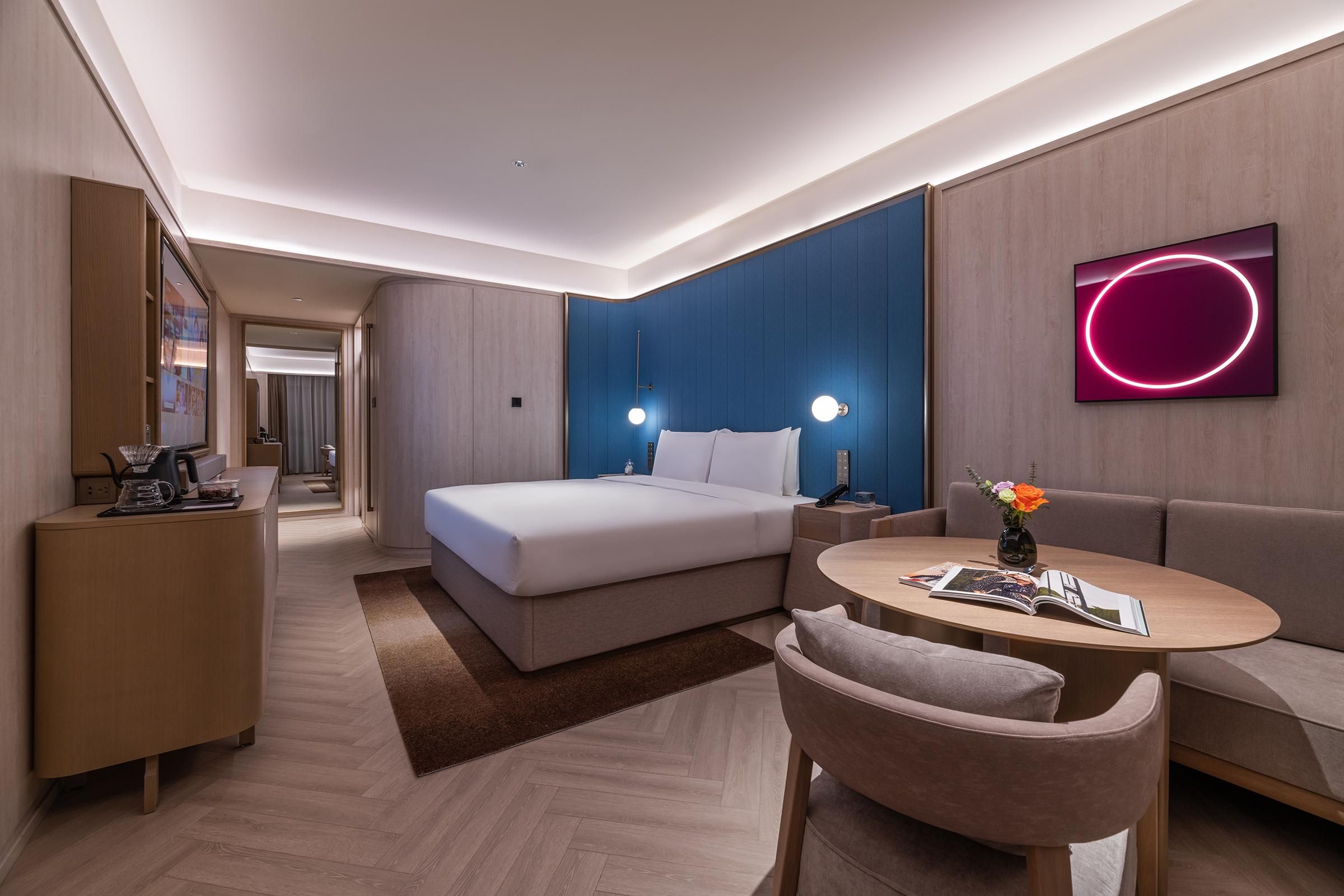 A modern hotel room with a bed, a sofa, a small table, and a TV.