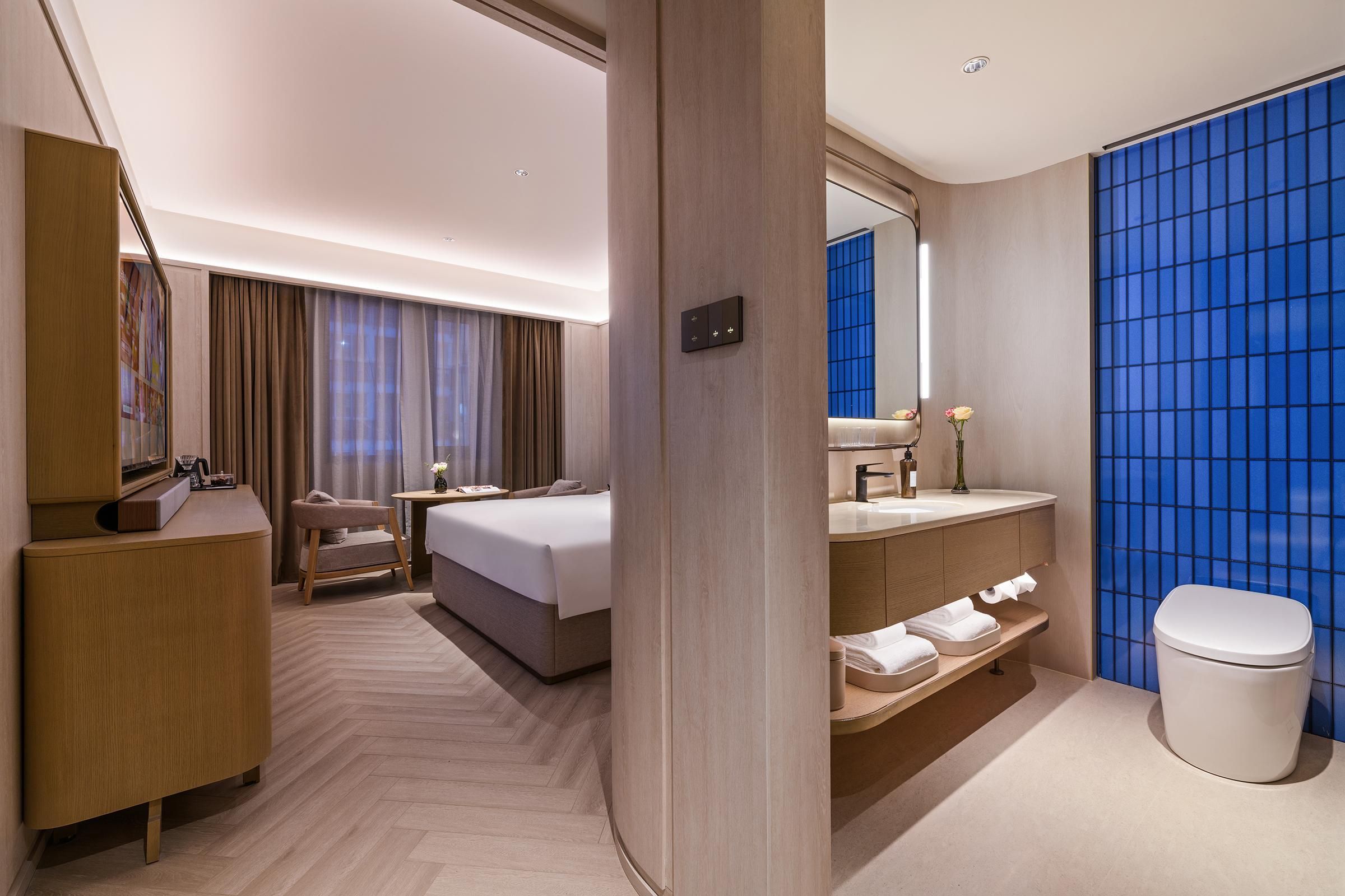 Una habitación de hotel moderna con una cama, un escritorio, un tocador con espejo y un baño con inodoro y lavabo.