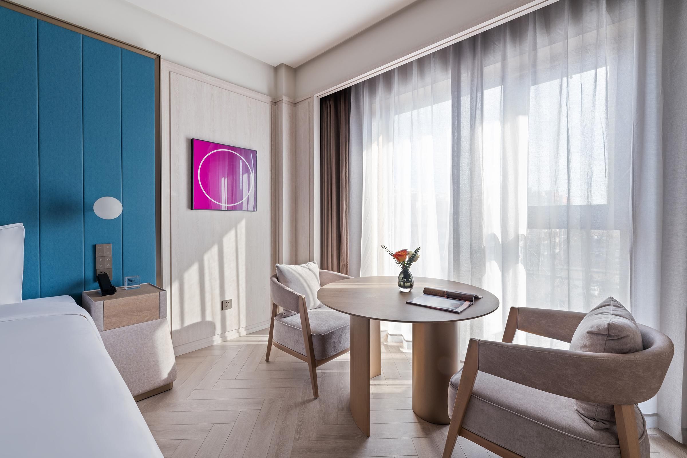 A hotel room with a bed, a desk with a phone, a chair, a table, and a window with curtains.