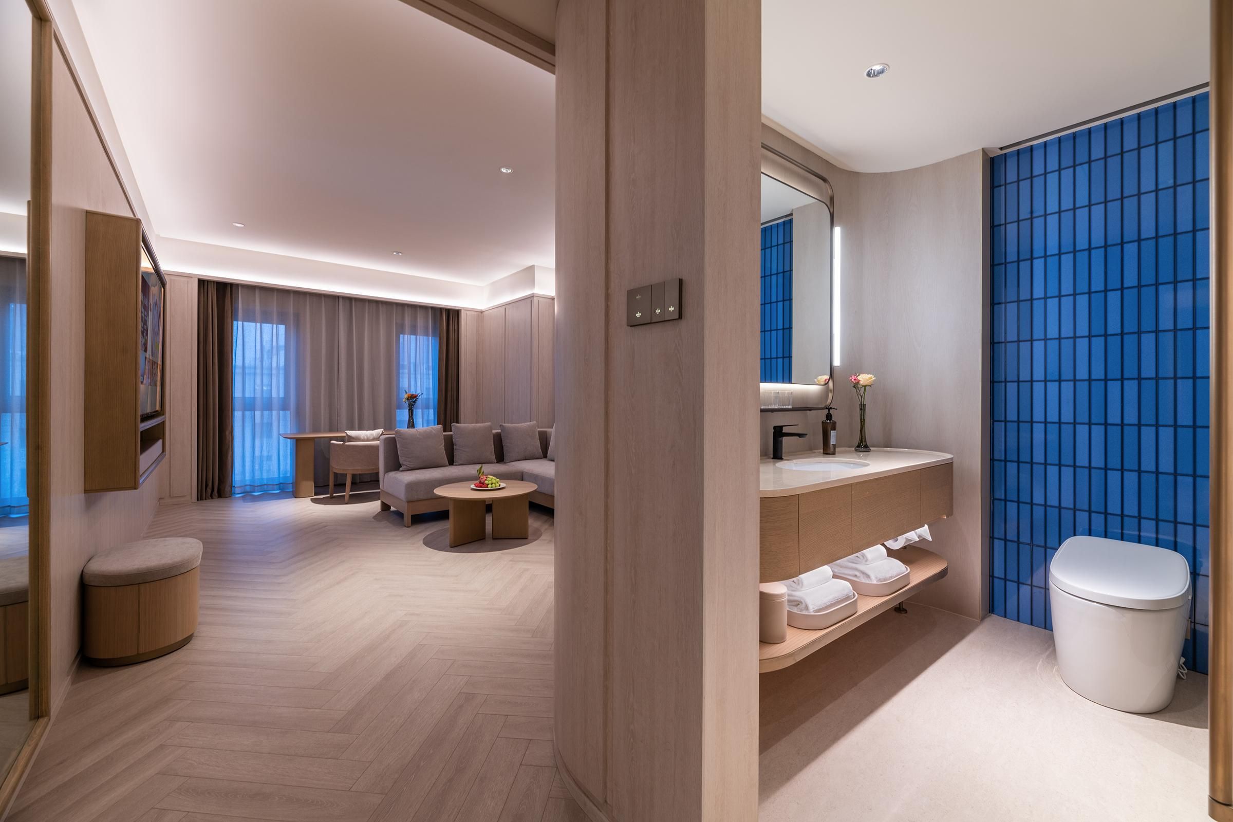 A modern hotel room with a sofa, coffee table, and a bathroom with a blue tiled wall.