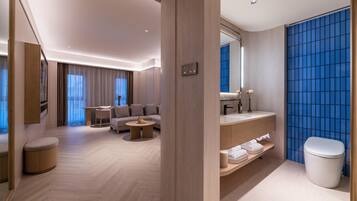 A modern hotel room with a sofa, coffee table, and a bathroom with a blue tiled wall.