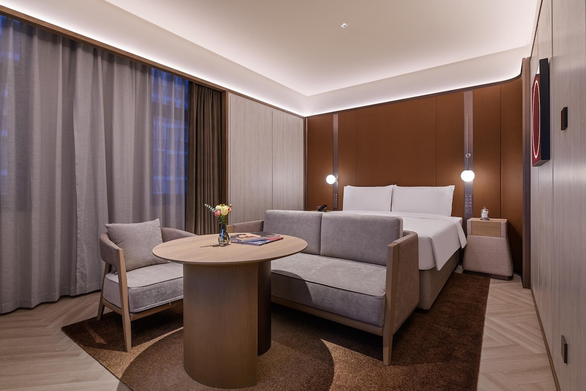 Una habitación de hotel moderna con un sofá, una mesita, una mesita de noche y una cama.