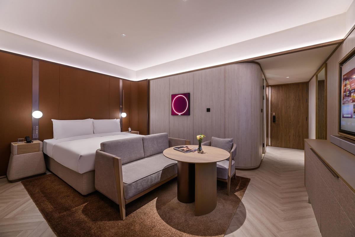 Une chambre d’hôtel moderne équipée d’un lit, d’un canapé, d’une table ronde et d’un téléviseur fixé au mur.