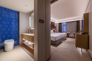 Una habitación de hotel moderna con una cama grande, un escritorio, una silla, un baño con inodoro y una pared con azulejos azules.