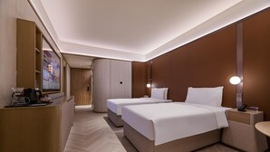 Hotellihuone, jossa on kaksi sänkyä, työpöytä, peili ja seinälle asennettu televisio.