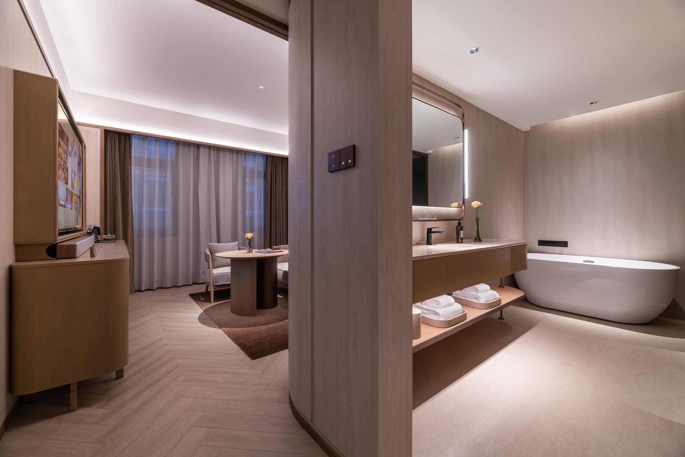 A modern hotel room with a large bathtub, a vanity with a mirror, a desk, and a chair.