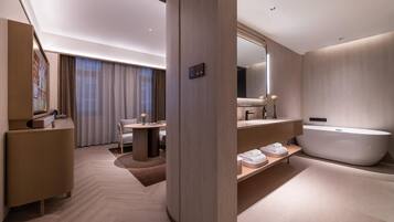 A modern hotel room with a large bathtub, a vanity with a mirror, a desk, and a chair.