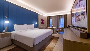 A modern hotel room with a large bed, a desk, a TV, and a seating area.