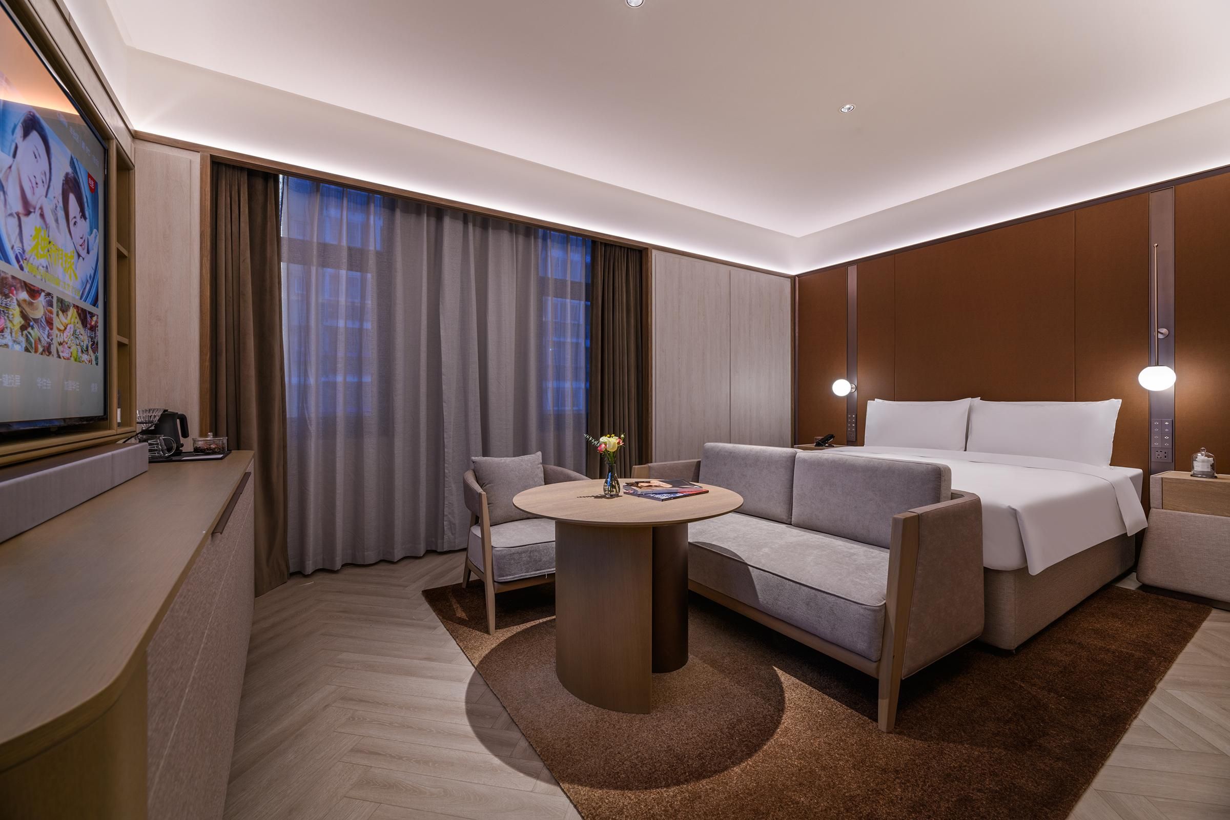 A modern hotel room with a sofa, a bed, a round table, and a TV.