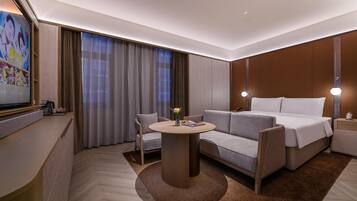 A modern hotel room with a sofa, a bed, a round table, and a TV.
