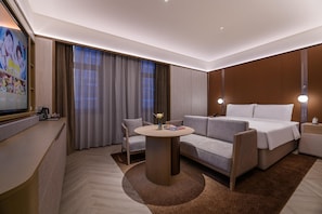 Una habitación de hotel moderna con sofá, cama, una mesa redonda y televisión.