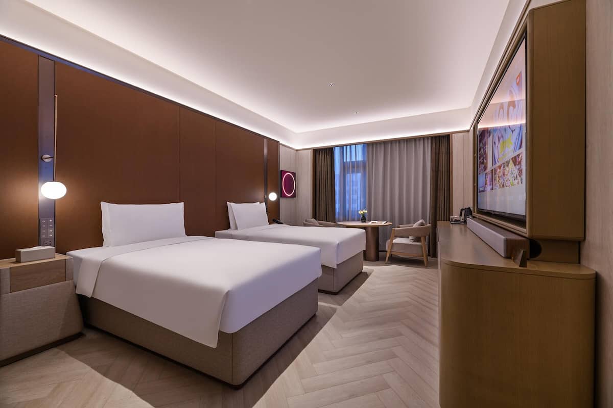 Une chambre d’hôtel avec deux lits, un bureau, une chaise, une télévision et une grande fenêtre avec des rideaux.