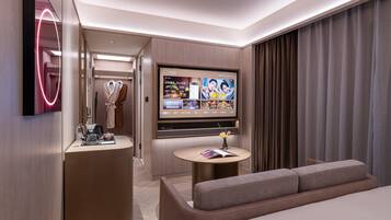 Una habitación de hotel moderna con un televisor de pantalla plana en la pared, una mesa de centro redonda, un sofá y un vestidor con batas colgadas.